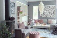 a glam living room with grey walls, grey sofas and a loveseats, pink pillows and a pouf and a large chandelier