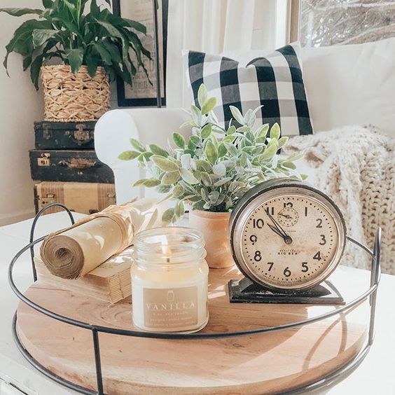 a glass tray with a large candle in a mason jar, a vintage clock, potted greenery and some old books