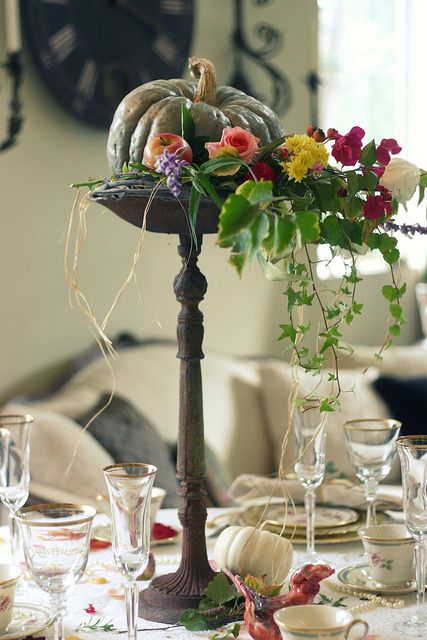 a heirloom pumpkin with faux apples and bright cascading blooms and greenery ona dark wooden stand is a lovely centerpiece