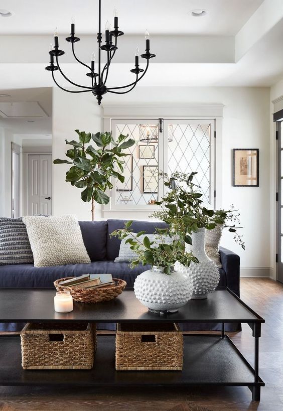 A large black coffee table with basket boxes, white vases with greenery, a woven catch all and a candle