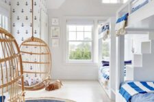 a light-filled beach kids’ room with built-in bunk beds with blue bedding, hanging egg-shaped chairs and a woven rug