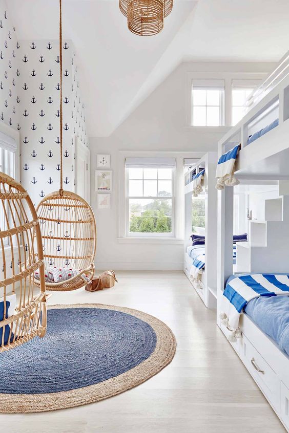 a light-filled beach kids' room with built-in bunk beds with blue bedding, hanging egg-shaped chairs and a woven rug