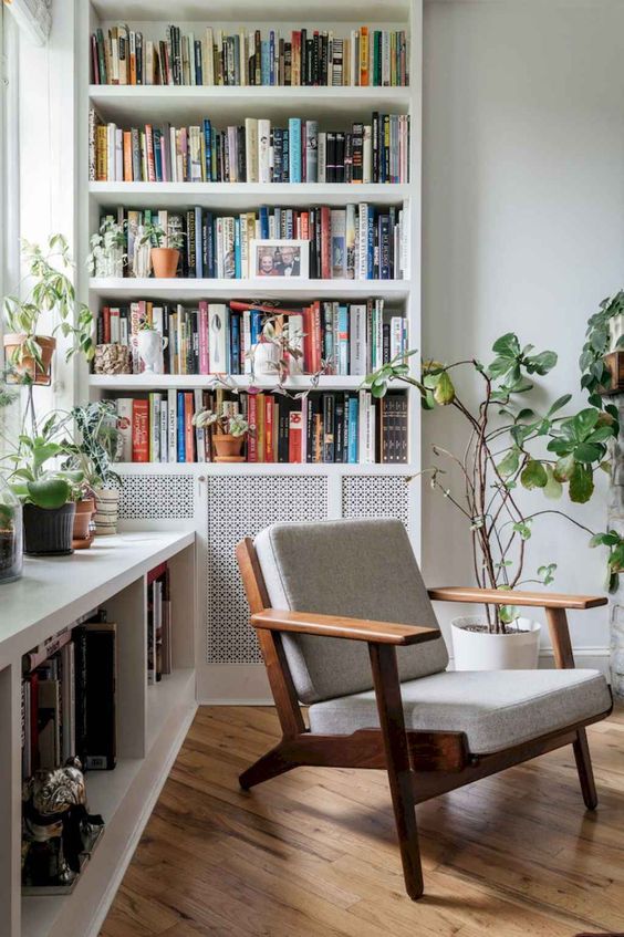 a lovely home library nook with a large bookcase and a large shelf by the window plus a chair