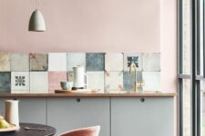 a lovely kitchen with pink walls, grey cabinets, a mismatching tile backsplash and pink chairs is super cool