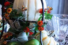 a metal tiered stand with hay, faux veggies and fruits and bright blooms plus large pumpkins for fall decor