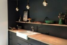 a minimalist black kitchen spruced up with a white sink and a wooden shelf plus countertops for a fresh look
