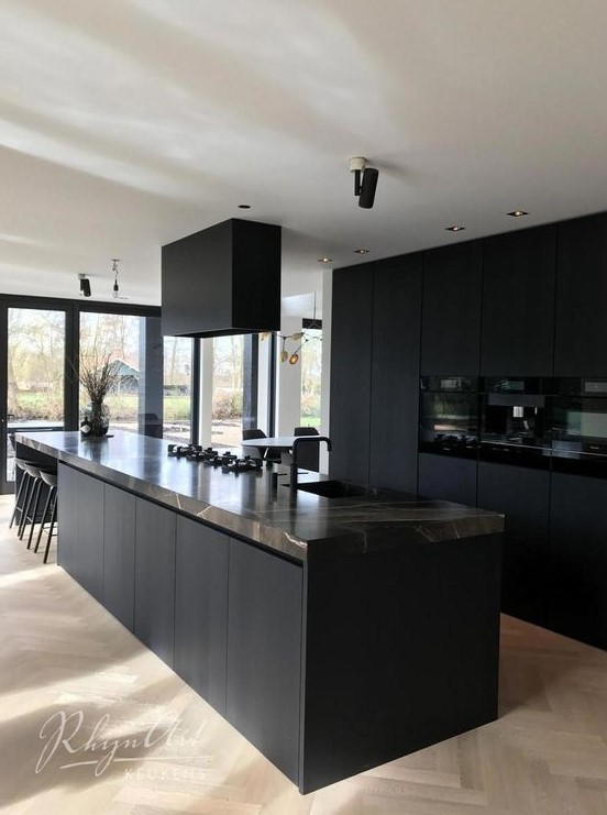 a minimalist black kitchen with sleek cabinets, a brown marble countertop plus a black hood
