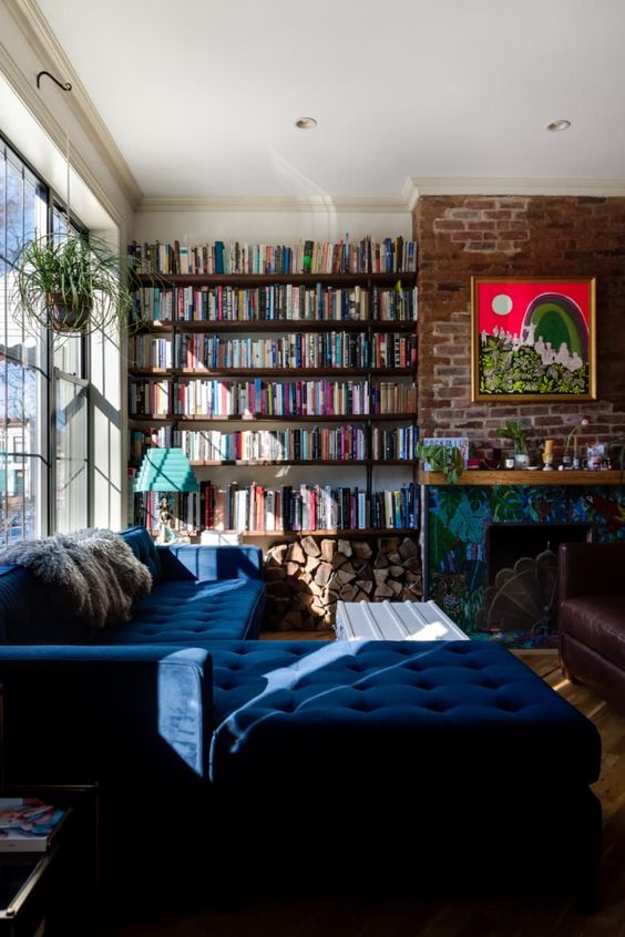A modern and bold home library with dark floating shelves, a navy L shaped sofa and a bold artwork