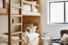 a modern and chic kids’ space with stained wood bunk beds with a ladder, a leather chair, neutral bedding and a printed rug