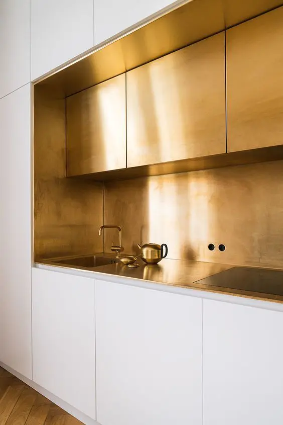 a modern glam kitchen with white and brass cabinets, a brass backsplash and countertops plus fixtures for a wow look
