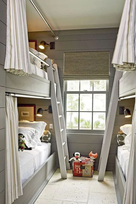 A modern grey kids' room with built in bunk beds, neutral and grey bedding, ladders and striped curtains plus black sconces