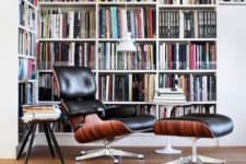 a modern home library nook with an oversized L-shaped bookcase, a black leather chair with a footrest