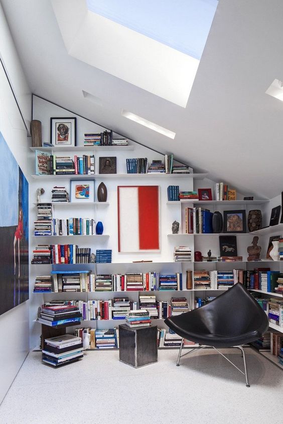 a modern home library with a skylight, some floating bookshelves and a black leather chair