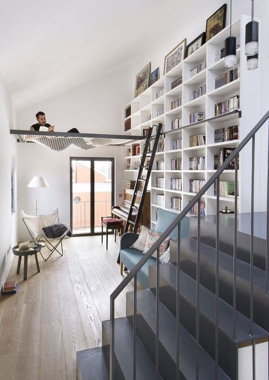 a modern home library with a white bookshelf unit, stairs, comfy chairs and a net for relaxing there
