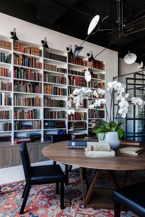 a modern home library with built-in bookshelves in white and a large round table and black leather chairs