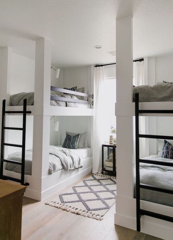 A modern kids' room with built in bunk beds, black ladders, a mirror cabinet, a printed rug and neutral bedding