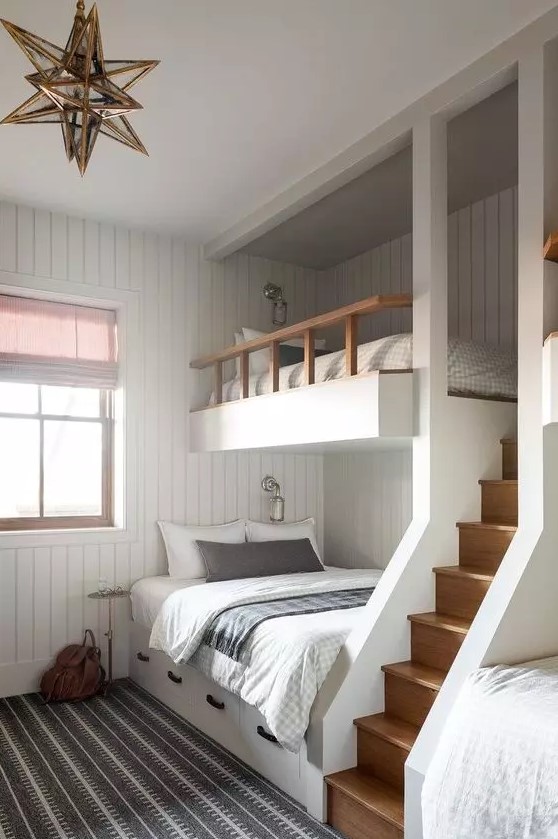 A modern kids' room with white shiplap walls, built in bunk beds with printed bedding, a gold star shaped pendant lamp and a ladder