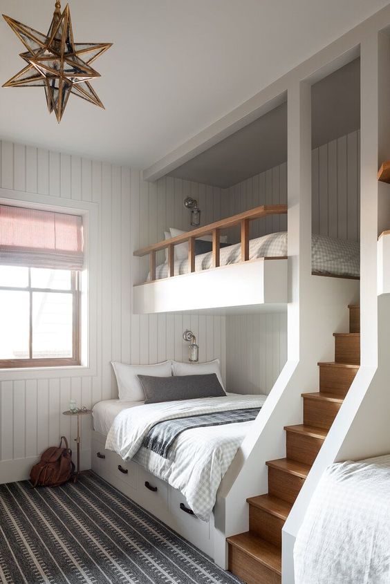 A modern kids' room with white shiplap walls, built in bunk beds with printed bedding, a gold star shaped pendant lamp and a ladder