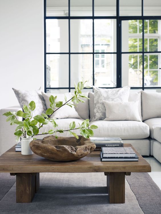 a modern rustic coffee table with a rough wooden bowl, books and a greenery arrangement in a vase