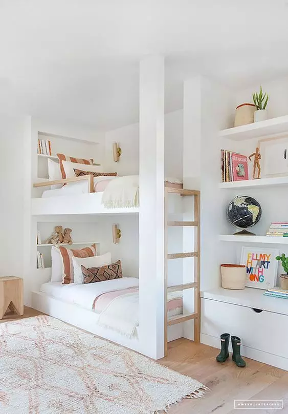 A modern white bedroom with built in bunk beds, a ladder, built in shelves and a small wooden stool is a stylish light filled space for kids