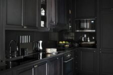a moody black kitchen with shaker cabinets, a black backsplash and countertops, black fixtures is a cool and chic space