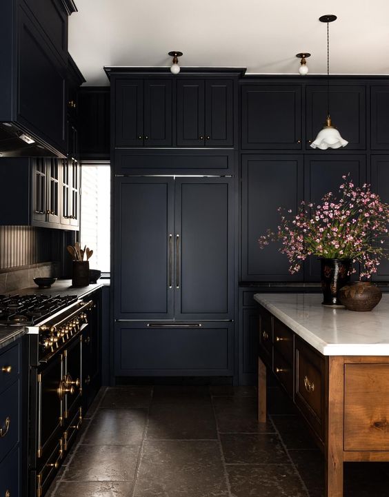 A moody kitchen with black shaker cabinets, a rich stained kitchen island, a vintage style black cooker and touches of brass