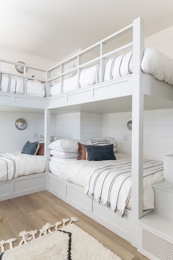 a neutral coastal kids' room with built-in bunk beds, neutral bedding, a built-in ladder and seaside-inspired sconces