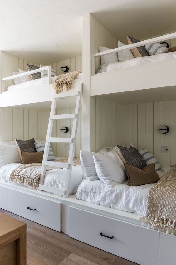 a neutral farmhouse kids' bedroom with shiplap walls, built-in bunk beds, neutral bedding and a ladder plus wall sconces