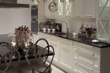 a neutral glam kitchen with black countertops, shiny silver stools, a crystal chandelier and pink florals