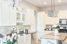 a neutral glam kitchen with white cabinetry, grey stone countertops, shiny crystal chandeliers and grey tiles