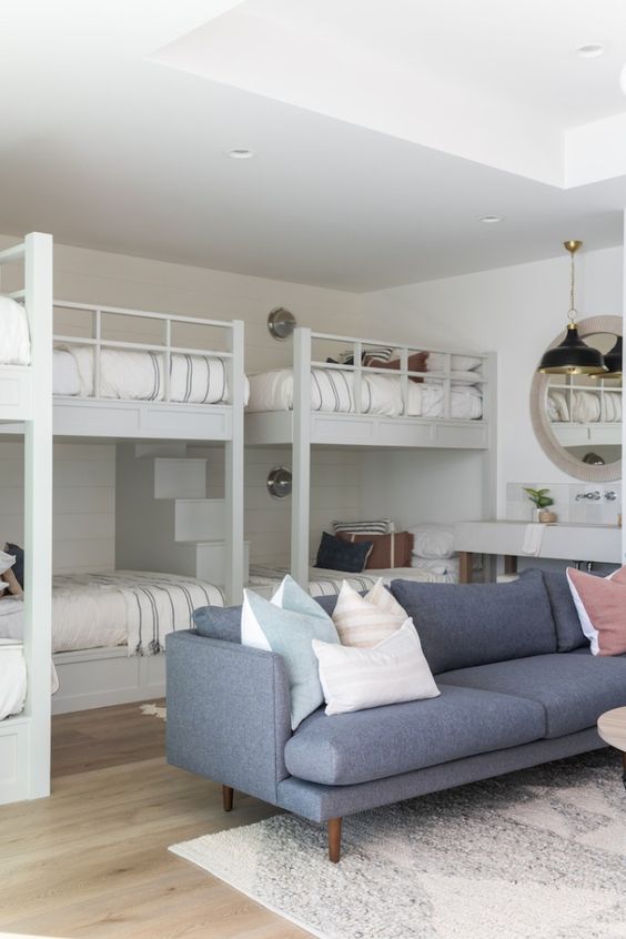 a neutral kids' bedroom with built-in bunk beds and a ladder, neutral bedding, a grey sofa and pillows, a console table