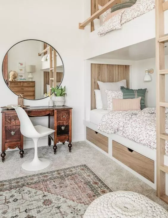 A neutral modern kids' room with built in bunk beds, printed bedding, a vintage stained desk and a round mirror, printed rugs