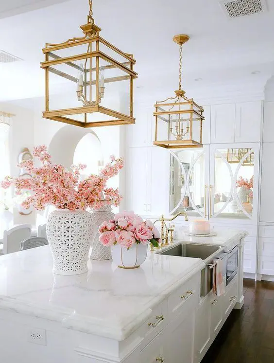 a neutral vintage glam kitchen with white cabinetry, touches of mirror, white marble countertops, gold handles and gold cage chandeliers
