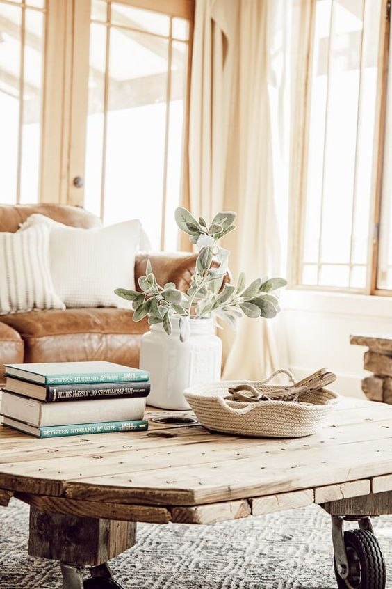 a reclaimed wood coffee table, a woven tray, a white vase with greenery and a stack of books