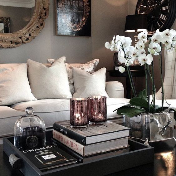 a refined coffee table arrangement with potted white orchids, a stack of books, a candle and a black tray