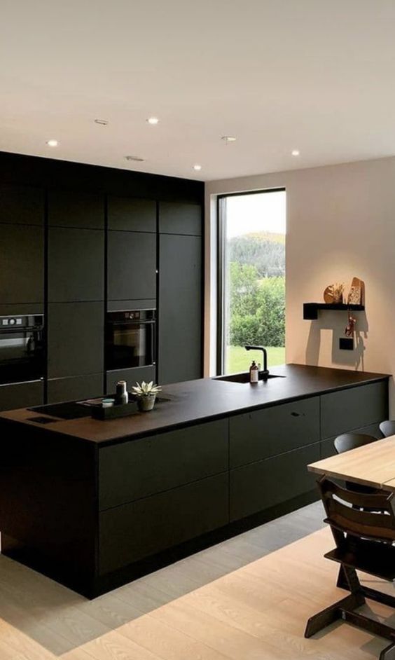 A refined minimalist black kitchen with sleek cabinets, brown countertops, built in appliances and a small dining space