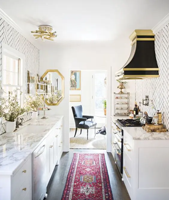 a retro glam kitchen with white cabinets, white marble countertops and a white tile backsplash, a black hood and gold touches