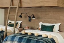 a rustic kids’ room with a wood clad accent wall and bunk beds, printed bedding, black lamps is a very cozy space