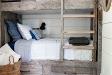 a rustic kids’ room with aged reclaimed kids’ bunk beds, printed and neutral bedding, a basket with bedding and black sconces on the walls