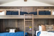a rustic kids’ room with stained bunk beds and an accent wall, a ladder, navy, blue and white bedding and a printed rug