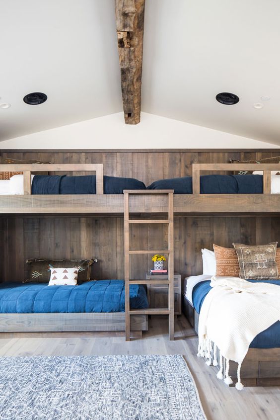 a rustic kids' room with stained bunk beds and an accent wall, a ladder, navy, blue and white bedding and a printed rug