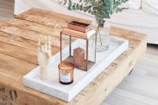 a rustic wooden coffee table with a marble tray, a copper lantern, a candle in a glass jar, eucalyptus in a clear vase