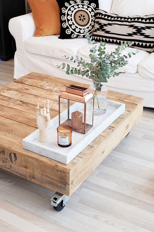 a rustic wooden coffee table with a marble tray, a copper lantern, a candle in a glass jar, eucalyptus in a clear vase