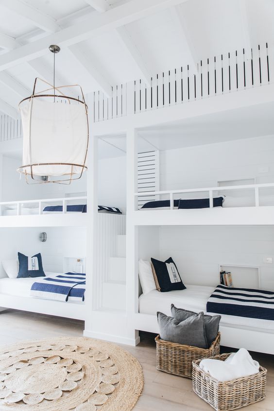 A seaside kids' room with built in white bunk beds with navy and white bedding, baskets for storage and a woven rug
