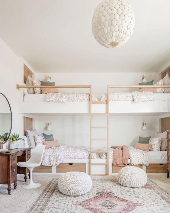 A serene kids' bedroom with built in bunk beds, printed bedding and a rug, poufs, a vintage vanity and a round mirror