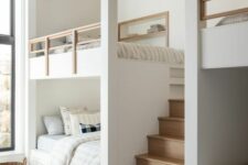 a serene neutral kids’ room with built-in bunk beds, neutral bedding, niches with shelves and a built-in stained ladder is chic