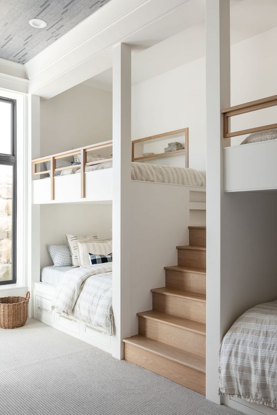 A serene neutral kids' room with built in bunk beds, neutral bedding, niches with shelves and a built in stained ladder is chic
