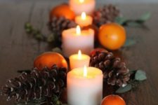 a simple and stylish fall centerpiece of pillar candles, pinecones, foliage and citrus is amazing for any party