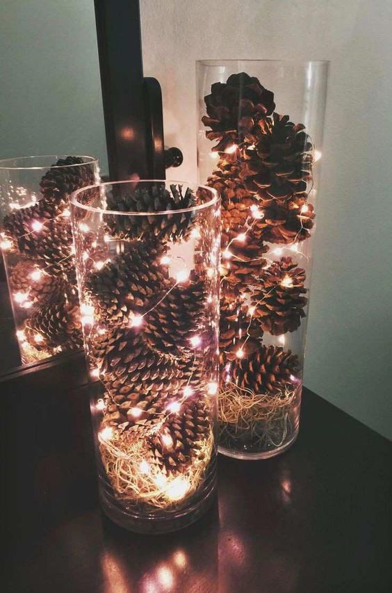 a simple modern fall centerpiece of clear vases with pinecones, hay and lights will fit any space