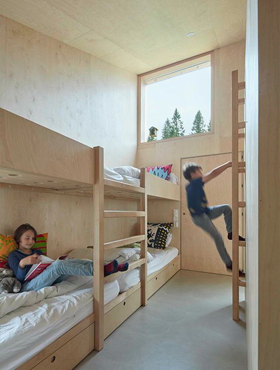 a simple modern kids' room with a built-in bunk bed with ladders, neutral and printed bedding and large windows